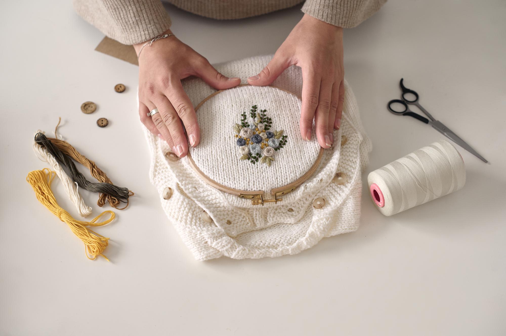 Artisan hands stitching a floral emblem on linen
